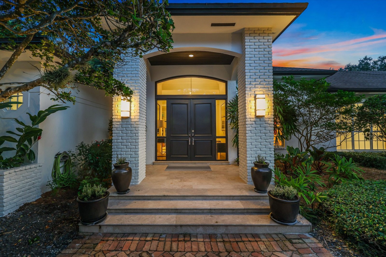 Covered entry with black double doors and white brick columns at twilight